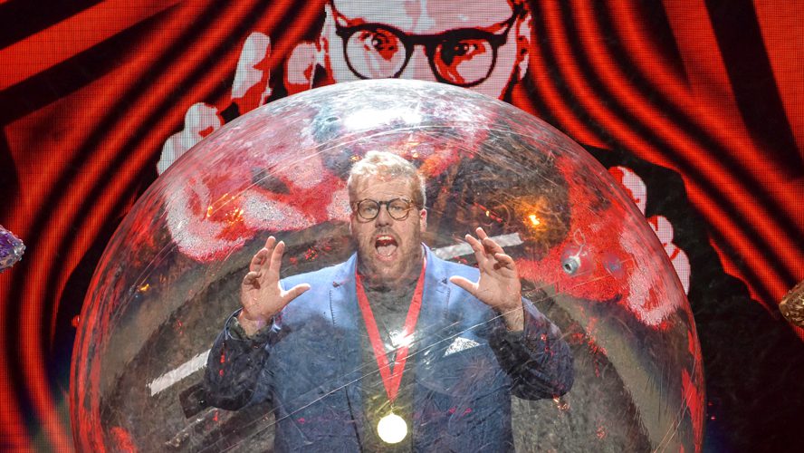 A magician performs on stage at the Apollo Theatre, surrounded by vibrant stage lights and props.