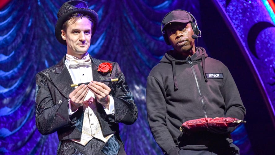 A stage scene from "Magic Goes Wrong" at the Vaudeville Theatre, featuring performers in vibrant costumes.