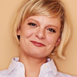 Martha Plimpton smiling, wearing a black top, with shoulder-length brown hair and natural makeup.