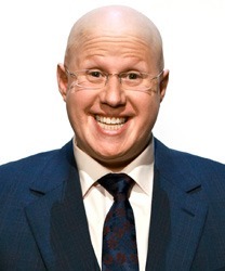 Matt Lucas smiling, wearing a dark suit and white shirt, with short, light brown hair.
