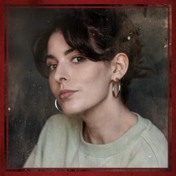 Woman with dark hair and hoop earrings, wearing a light top, framed in red.