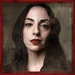 A woman with long dark hair and red lipstick, against a textured grey background.