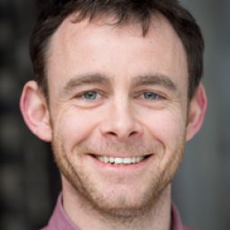 Mike Hugo smiling, wearing a navy suit and white shirt, with short brown hair.