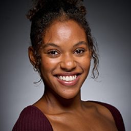 Nicole-Lily Baisden smiling, wearing a costume, with a magical backdrop from Harry Potter and the Cursed Child.
