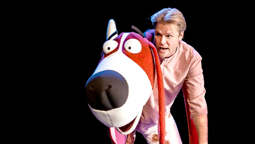 A vibrant stage scene featuring colourful animal puppets interacting with children in a lively performance.