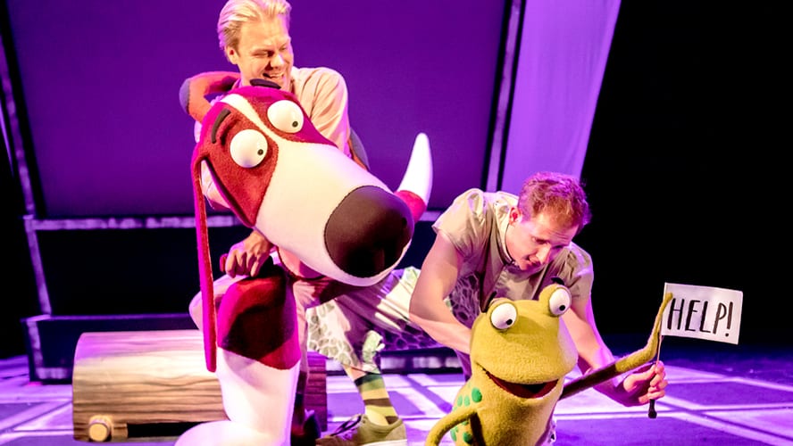 A vibrant stage scene featuring colourful animal puppets in a playful, whimsical setting.