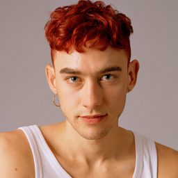 Olly Alexander performing on stage, wearing a stylish outfit, with dramatic lighting and a captivated audience.