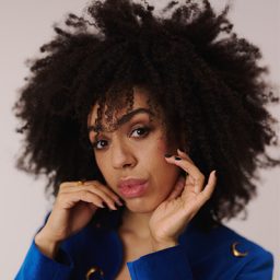 Pearl Mackie performing on stage, wearing a black outfit, with a spotlight illuminating her.