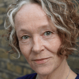 Penny Layden smiling, with shoulder-length hair, wearing a black top against a neutral background.