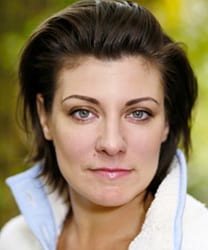 Polly Lister smiling, wearing a blue blouse, with shoulder-length brown hair and a neutral background.