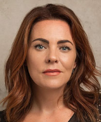 Rachel Tucker smiling, with long brown hair and wearing a black top against a neutral background.