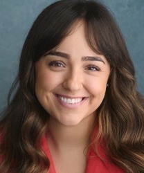 Rebecca Wickes smiling, wearing a blue blouse, with shoulder-length brown hair and a neutral background.