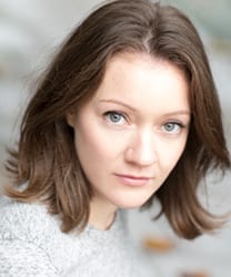 Rebecca Killick smiling, wearing a blue blouse, with shoulder-length brown hair and a neutral background.