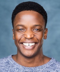 Rodney Vubya smiling, wearing a dark suit and tie, with a blurred background.