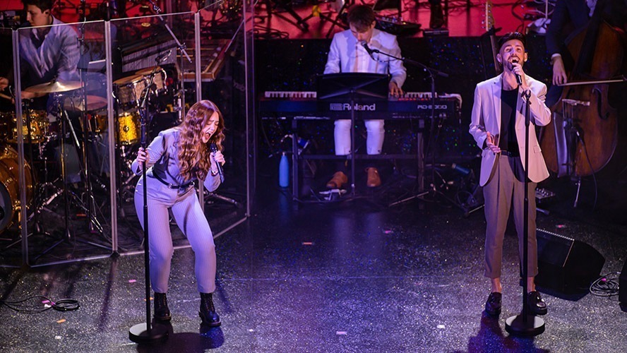 A group of actors in costume rehearsing a scene on stage with dramatic lighting.