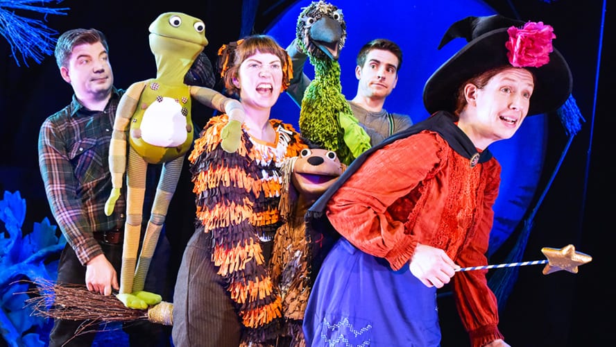 A whimsical scene featuring a witch, a dog, a cat, and a bird on a broomstick.