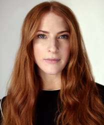 Rosalie Craig smiling, wearing a black dress with a floral pattern, against a neutral background.