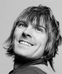 Ryan Farmery smiling, wearing a blue shirt, with a blurred outdoor background.