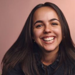 Jess with short dark hair, smiling, wearing a black top against a neutral background.