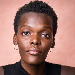 Sheila Atim standing on stage, wearing a black dress, with dramatic lighting illuminating her.