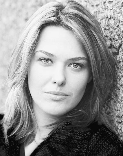 Sally Bretton smiling, with shoulder-length brown hair and wearing a black top against a neutral background.