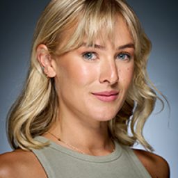 Sally-Jayne Hind smiling, wearing a black dress with a patterned shawl, against a neutral background.