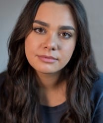 Sarah Seggari smiling, wearing a blue blouse, with long brown hair and a neutral background.