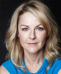 Sarah Hadland smiling, wearing a black top, with shoulder-length brown hair and a neutral background.