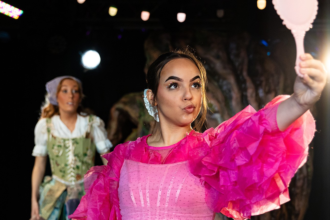 A vibrant stage scene featuring actors in dramatic costumes performing under colourful lighting.