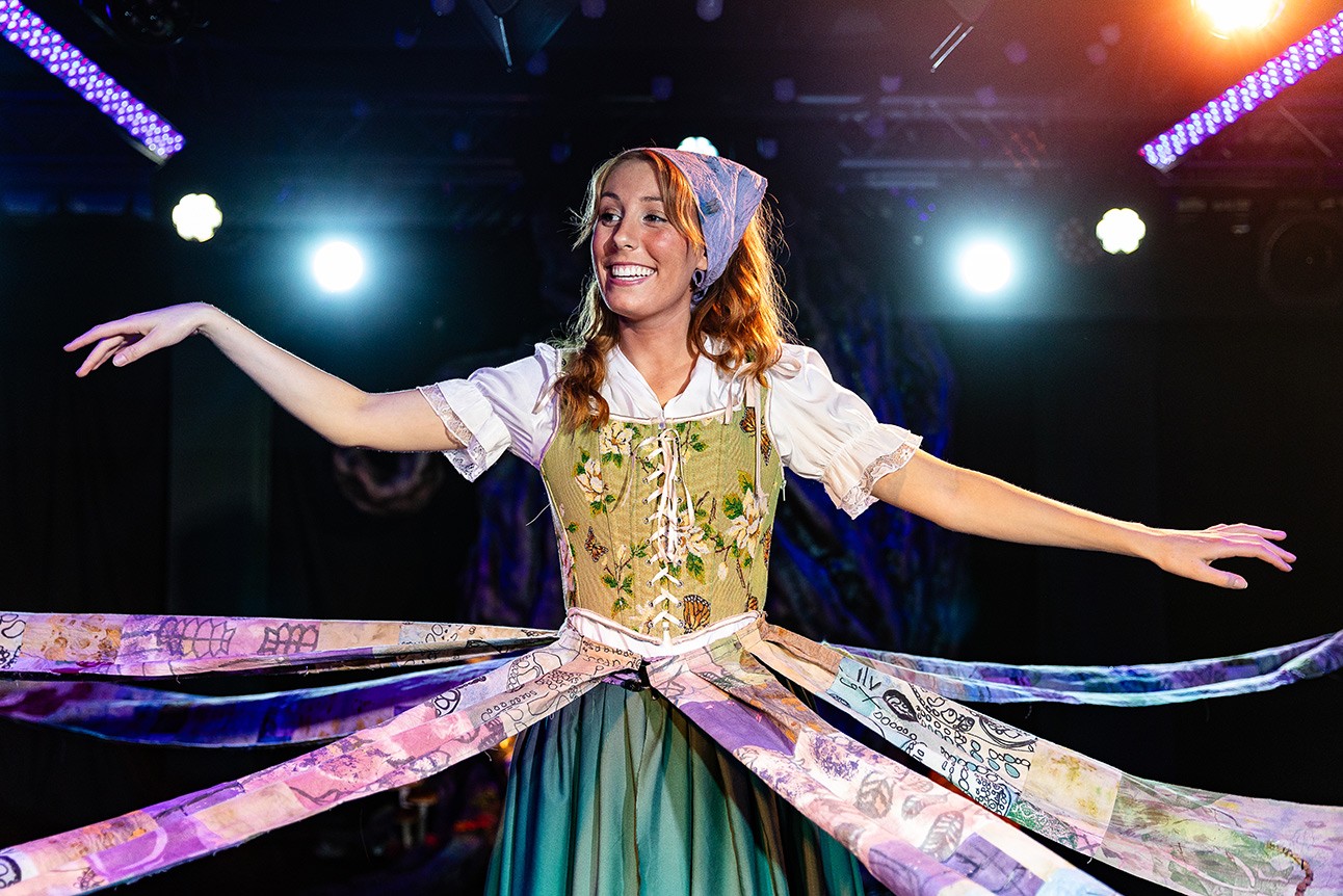 A stage scene featuring actors in dramatic costumes, surrounded by atmospheric lighting and props.