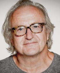 Simon Rouse smiling, wearing a dark suit and tie, with short brown hair and glasses.