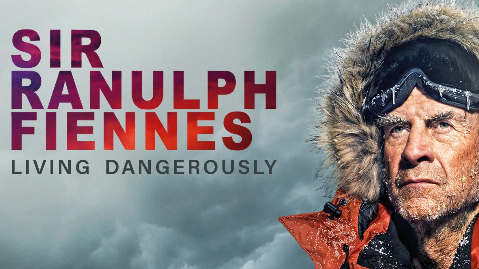 Sir Ranulph Fiennes smiling, wearing a dark jacket, with a blurred background of an outdoor setting.