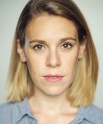 Steph De Whalley smiling, wearing a blue blazer and white blouse, with shoulder-length brown hair.
