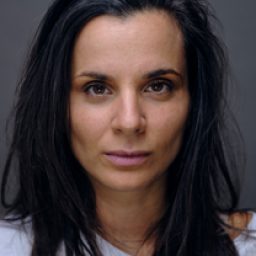 Suzanne Ahmet smiling, with shoulder-length dark hair and wearing a blue blouse against a neutral background.