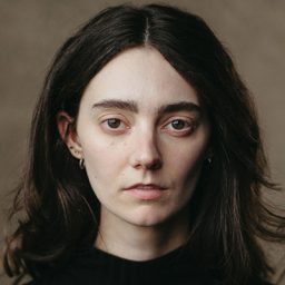 Tanya Reynolds smiling, wearing a black top, with long hair and a neutral background.