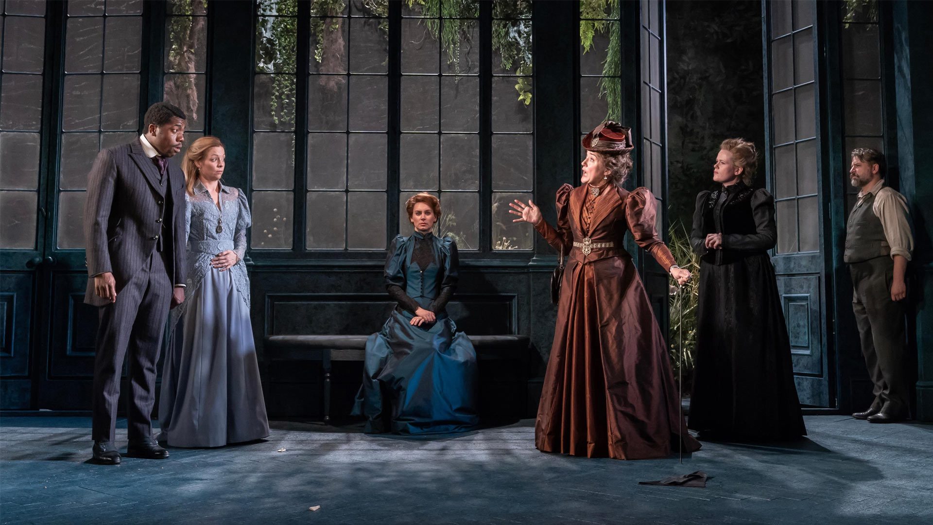 A theatrical scene from "The Importance of Being Earnest" featuring actors in Victorian costumes.