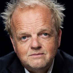 Toby Jones performing on stage, dressed in a black shirt, with dramatic lighting and a focused expression.