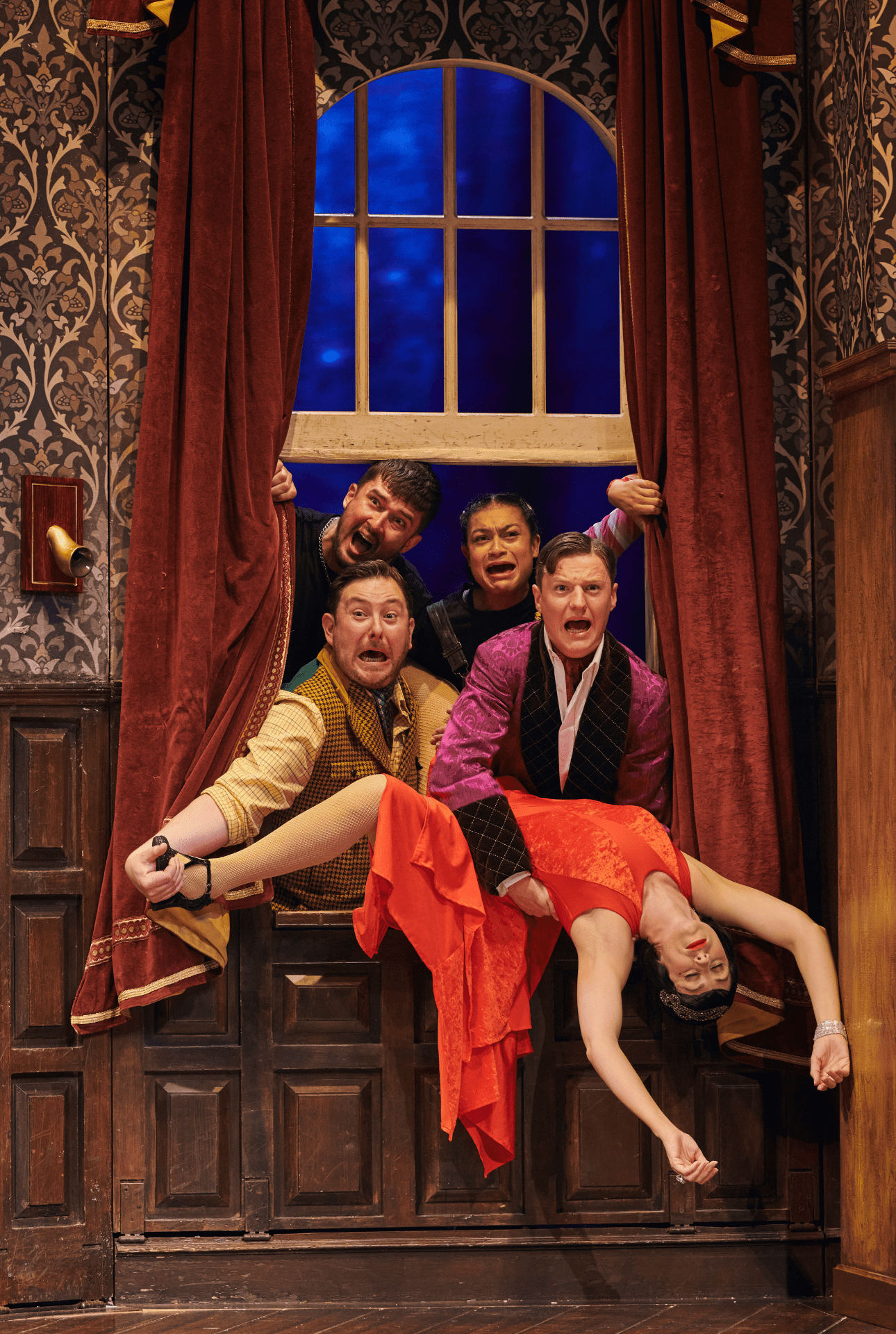 A stage scene from "The Play That Goes Wrong" featuring actors in comedic poses and costumes.