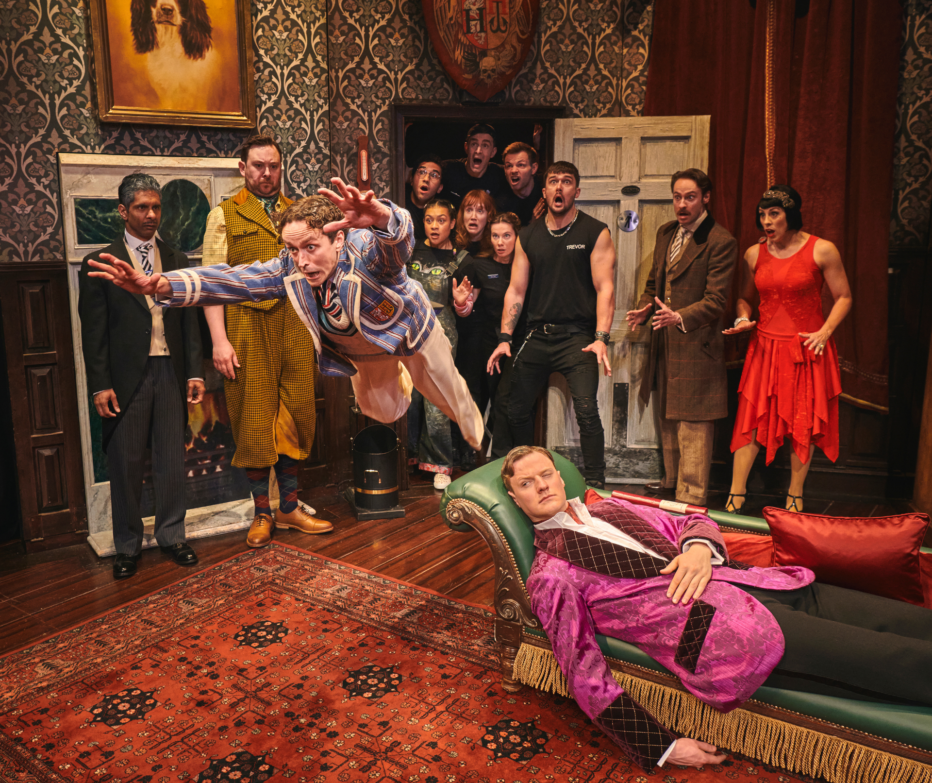 Group portrait of the cast from "The Play That Goes Wrong," smiling and posing together.