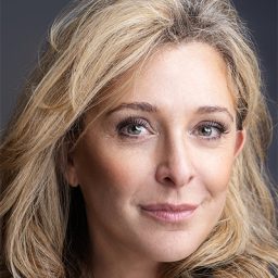 Tracy-Ann Obermann smiling, wearing a black top, with a blurred background.