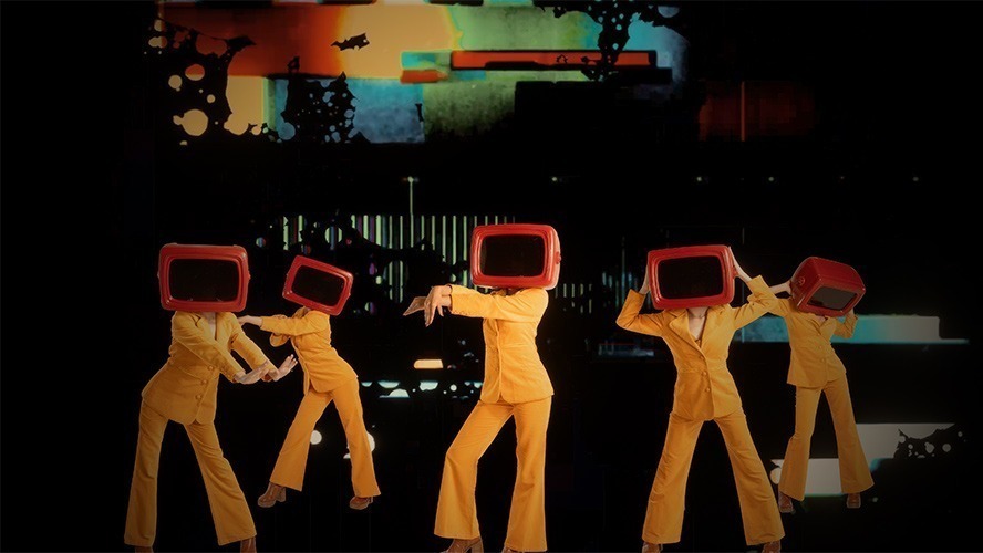 A vibrant stage scene featuring performers in colourful costumes, illuminated by dynamic lighting effects.