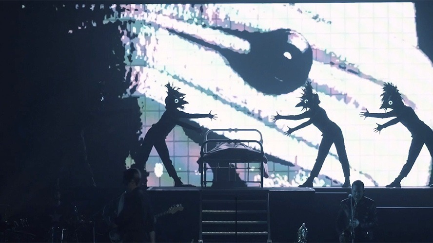 A vibrant stage scene featuring performers in striking costumes, illuminated by colourful stage lights.