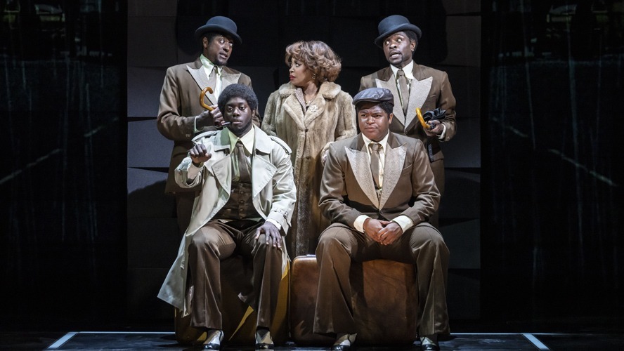 A vibrant stage scene featuring performers in 1960s attire, singing and dancing energetically.
