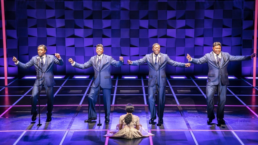 A vibrant stage scene featuring performers in 1960s attire, singing and dancing energetically.