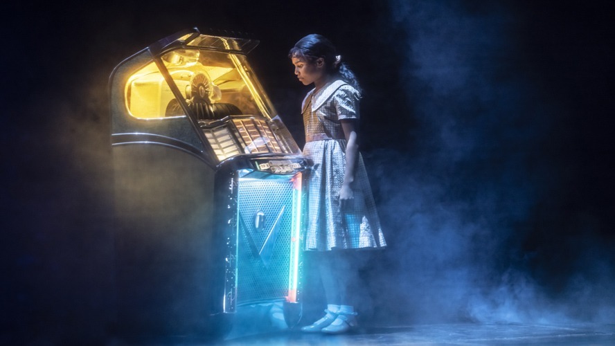 A vibrant stage scene featuring performers in colourful costumes, singing and dancing energetically.