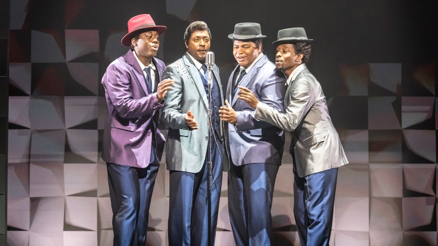 A vibrant stage scene featuring performers in stylish costumes, singing and dancing energetically.