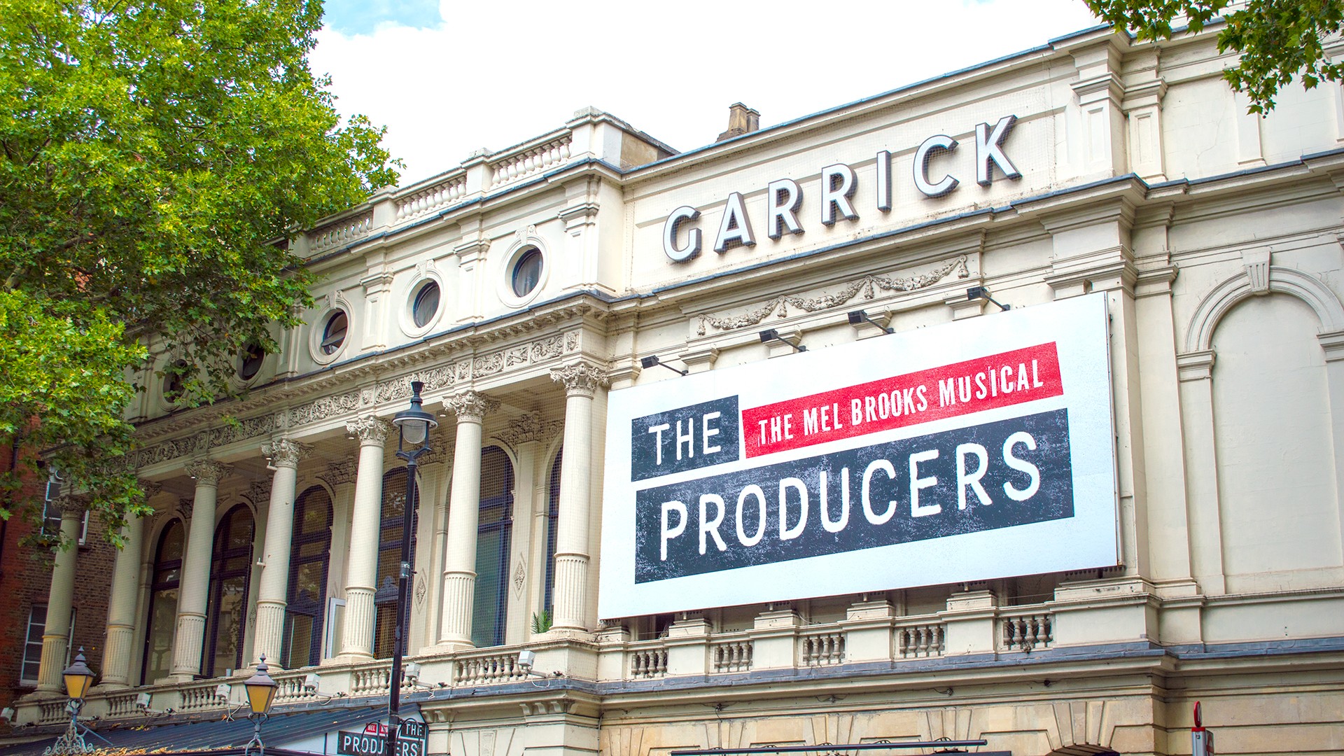 Garrick Theatre exterior featuring a marquee advertising "The Producers" with bright lights and vibrant colours.