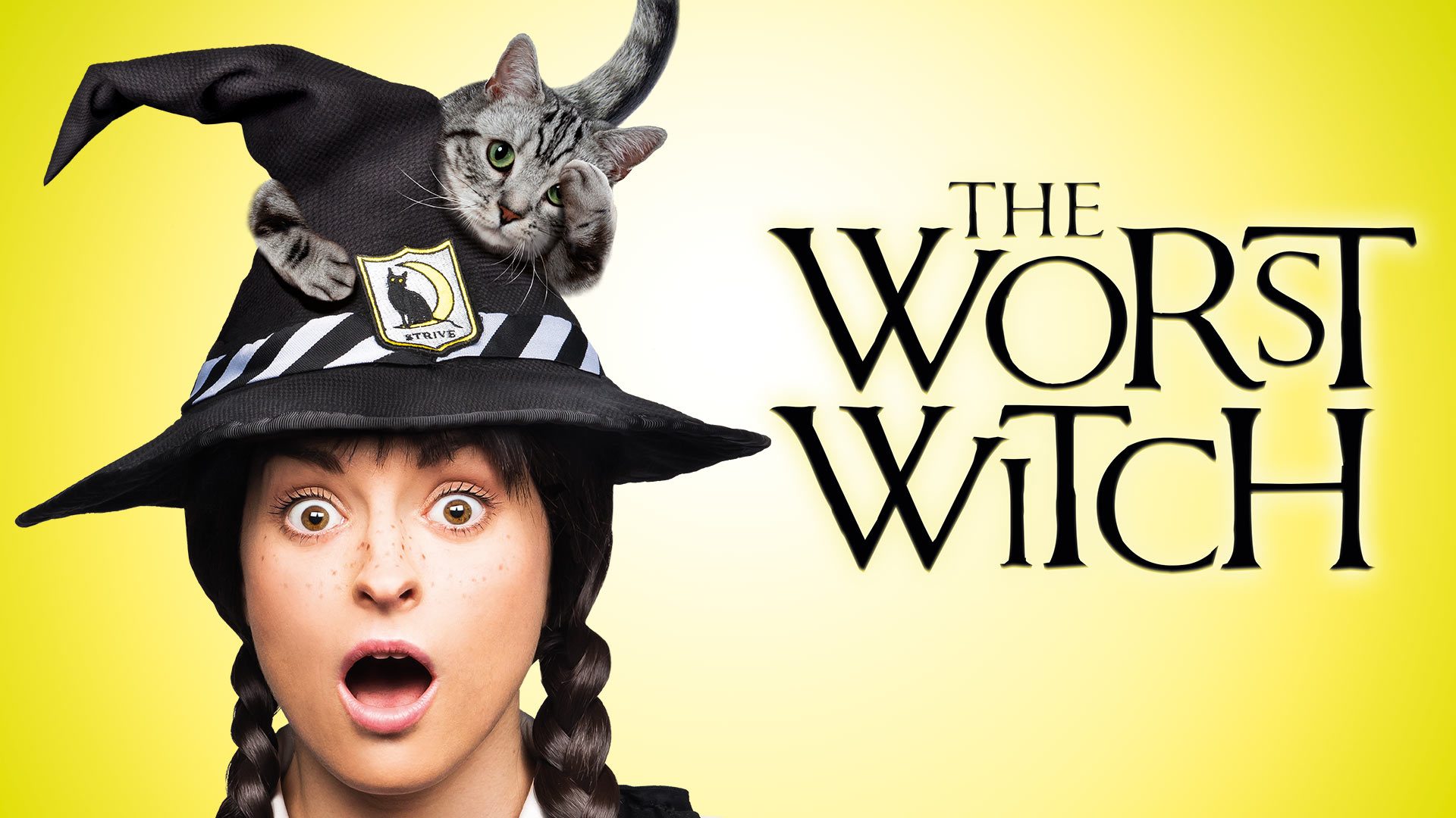 A young girl in a witch's outfit stands in a whimsical, enchanted classroom.