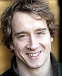 Thos Wainwright, a man with short dark hair, wearing a suit and tie, smiling confidently.