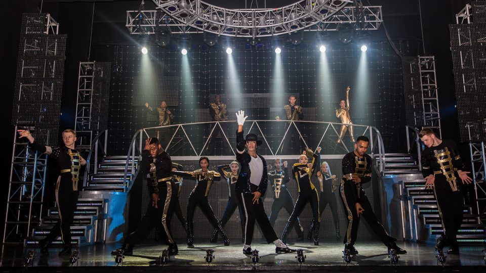 Dynamic stage performance featuring dancers in vibrant costumes, with dramatic lighting and energetic choreography.